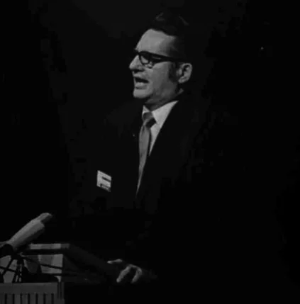 The founder of GEM in an older black and white photo. He is wearing a black suit and is in the midst of speaking into a microphone whilst looking off camera.