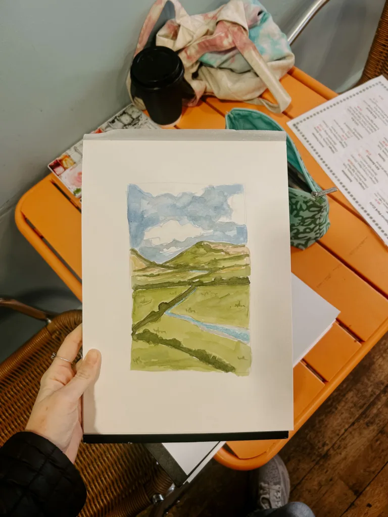 Hand holding a watercolor landscape painting created during outdoor park art ministry