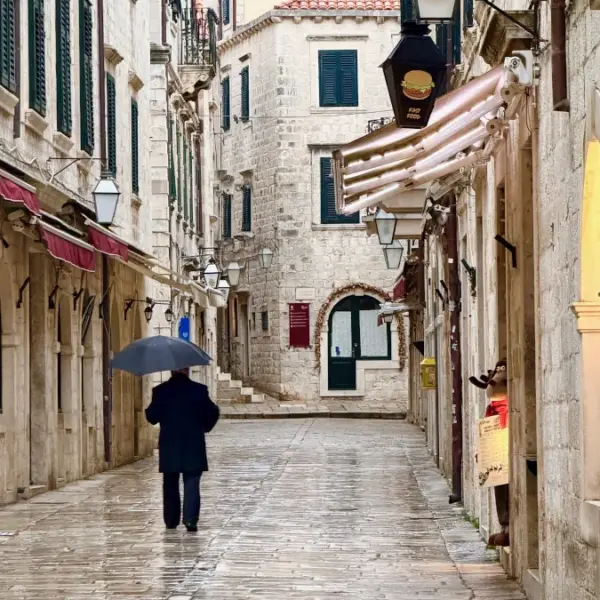 Person walking with an umbrella along a narrow stone street in historic Dubrovnik, Croatia
