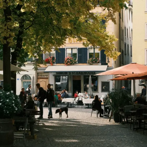 People gathered at outdoor cafés beneath autumn trees in a Swiss town square