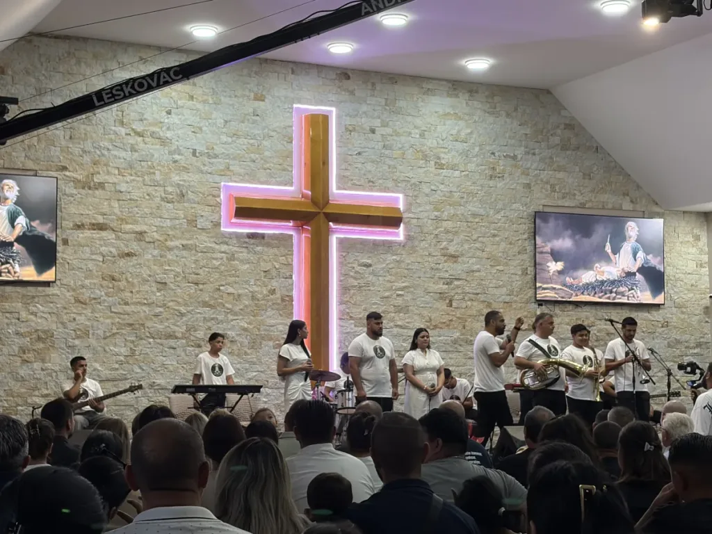 Worship team leading the congregation at Vitezda Church in Serbia beneath an illuminated cross.