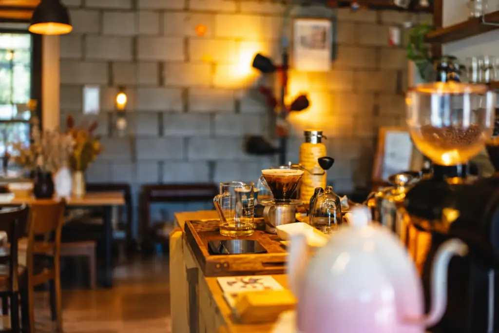 Pour-over coffee equipment and glass mugs arranged on a wooden café counter in warm, inviting light.